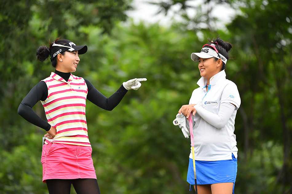 一名女球员正全神贯注地蹲在果岭上，用指尖轻轻放置一枚硬币标记，目光如炬地校准小球与球洞之间的精准位置。