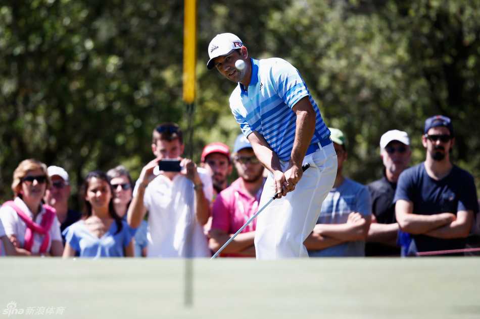 塞吉奥·加西亚在果岭边缘的长草中切球，他身体重心降低，眼神专注地锁定小白球，球杆即将触球瞬间，周围草地飞扬。