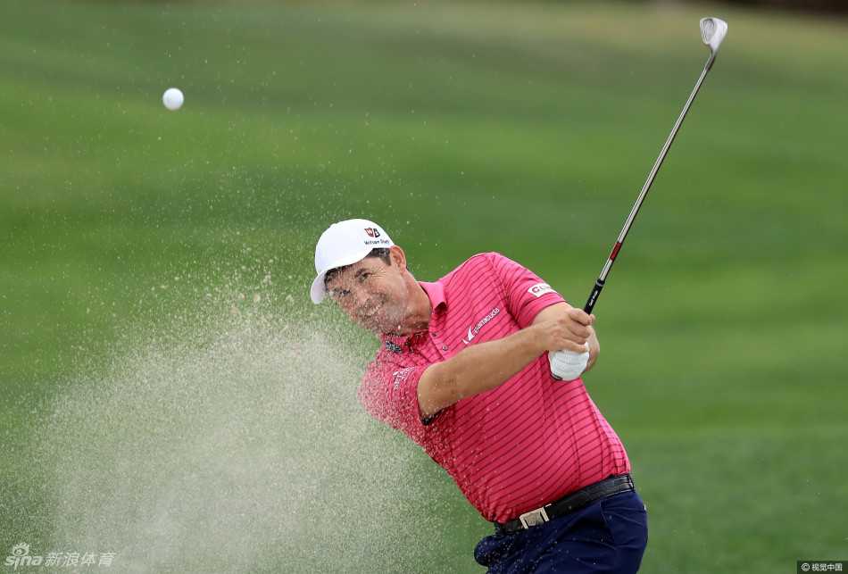 吉米·沃克尔站在球包旁，手持铁杆，正与球童认真讨论下一杆的选杆策略，表情严肃而专注。