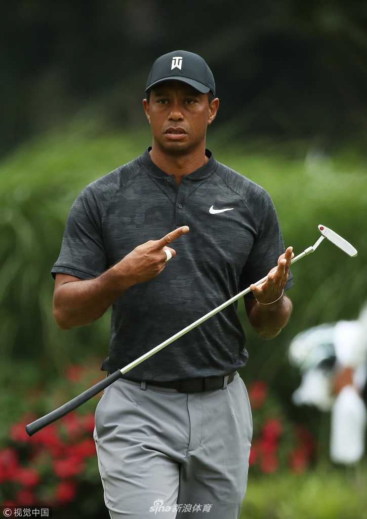 伍兹半蹲在果岭边，全神贯注地观察推杆线路，眼神锐利如鹰