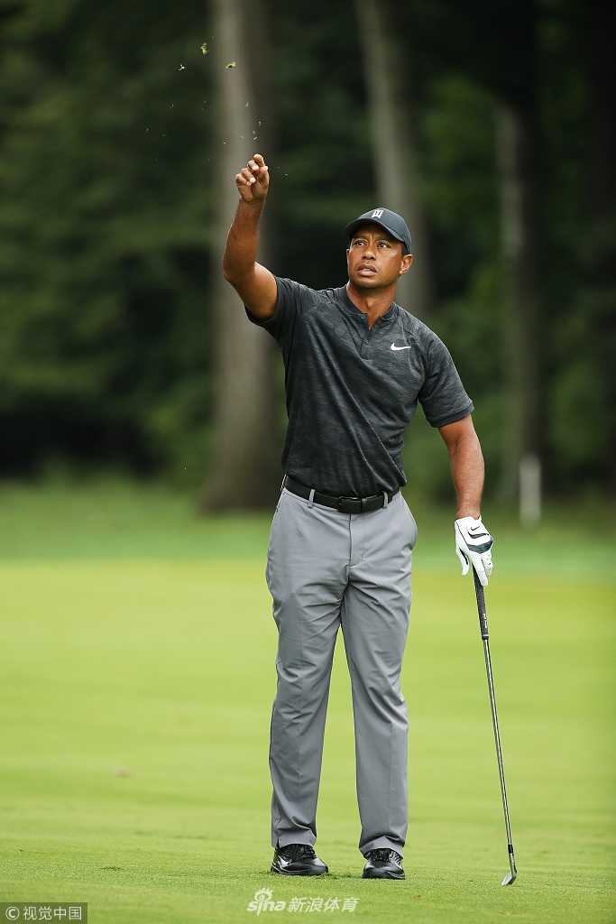 老虎伍兹身着红色Polo衫，在果岭上微笑着与球童交流，气氛轻松而自信
