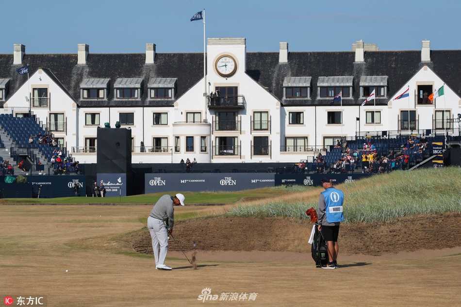 老虎伍兹在卡诺斯蒂宽阔的球道上使用长铁杆攻果岭，身体姿态舒展而有力，目光紧锁远处飘扬的旗杆。