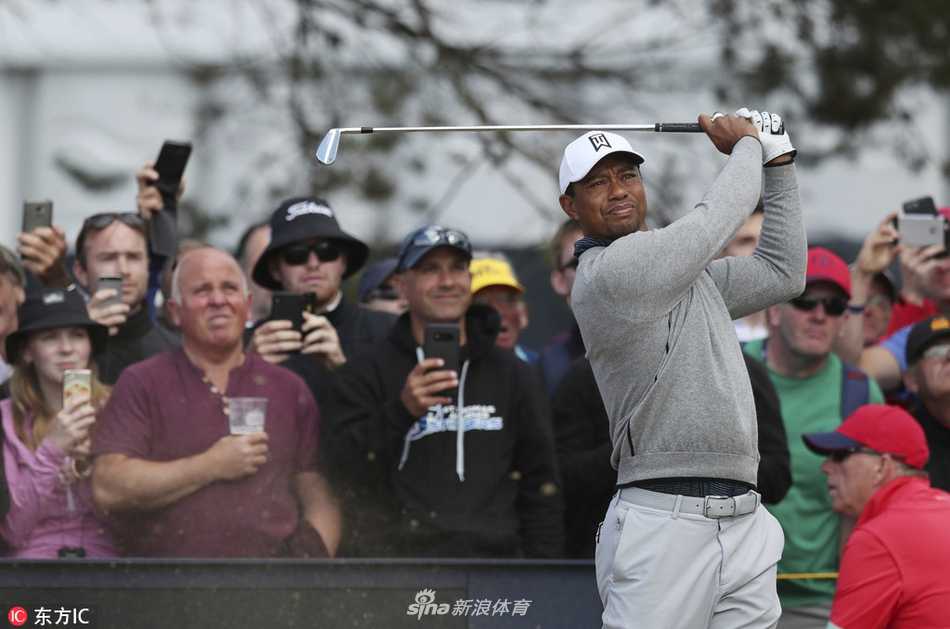 伍兹在练习日结束后向热情的支持者们挥手致意，脸上带着谦和的笑容，与身后卡诺斯蒂标志性的石桥与看台构成一幅经典画面。