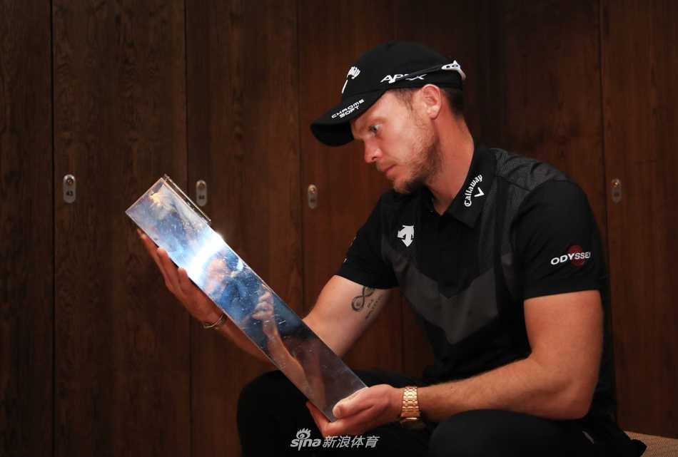 丹尼·威利特在第十八洞果岭上，沐浴着金色夕阳，坚定地推入锁定冠军的关键一推，身后是屏息凝神的观众。