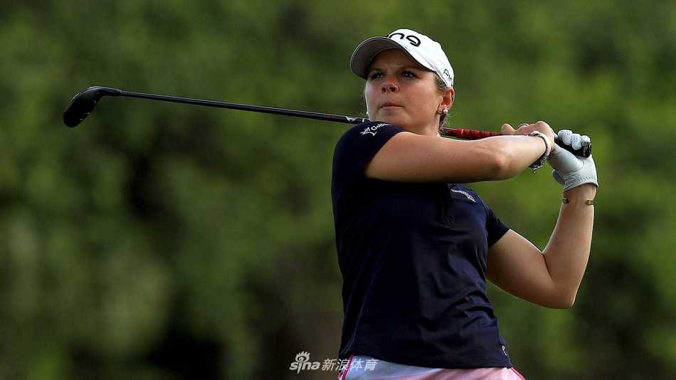 另一位球员在风中奋力挥杆击球，身体姿态展现出对抗风阻的全力爆发，背景中的观众正在凝神关注。