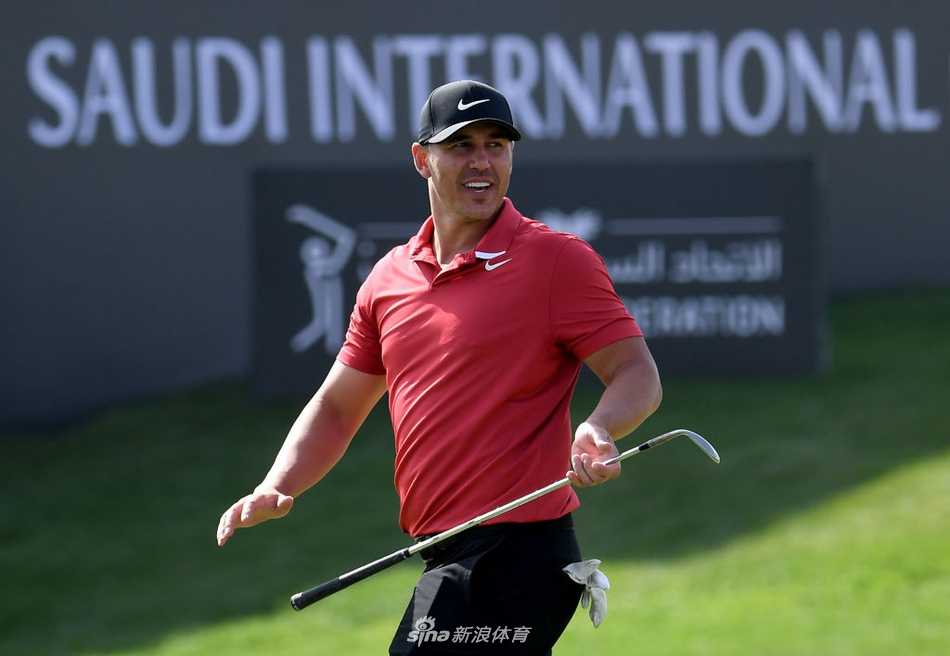 达斯汀·约翰逊在练习果岭边全神贯注地观察推杆线路，他身后巨大的赛事Logo在沙漠背景下格外醒目。