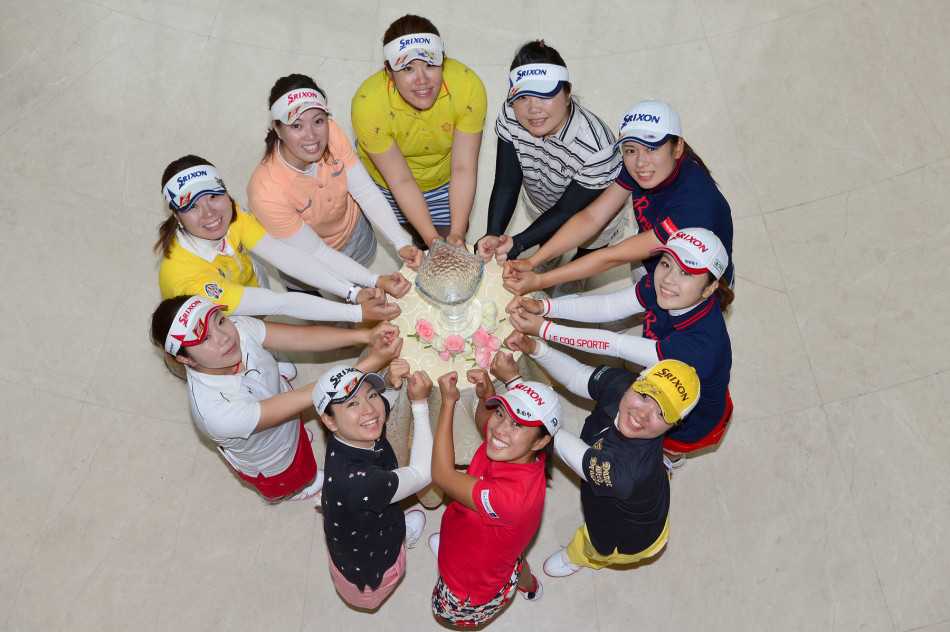 两位日韩女球员在果岭上低头细语，手轻抚推杆，神情专注中带着默契的微笑