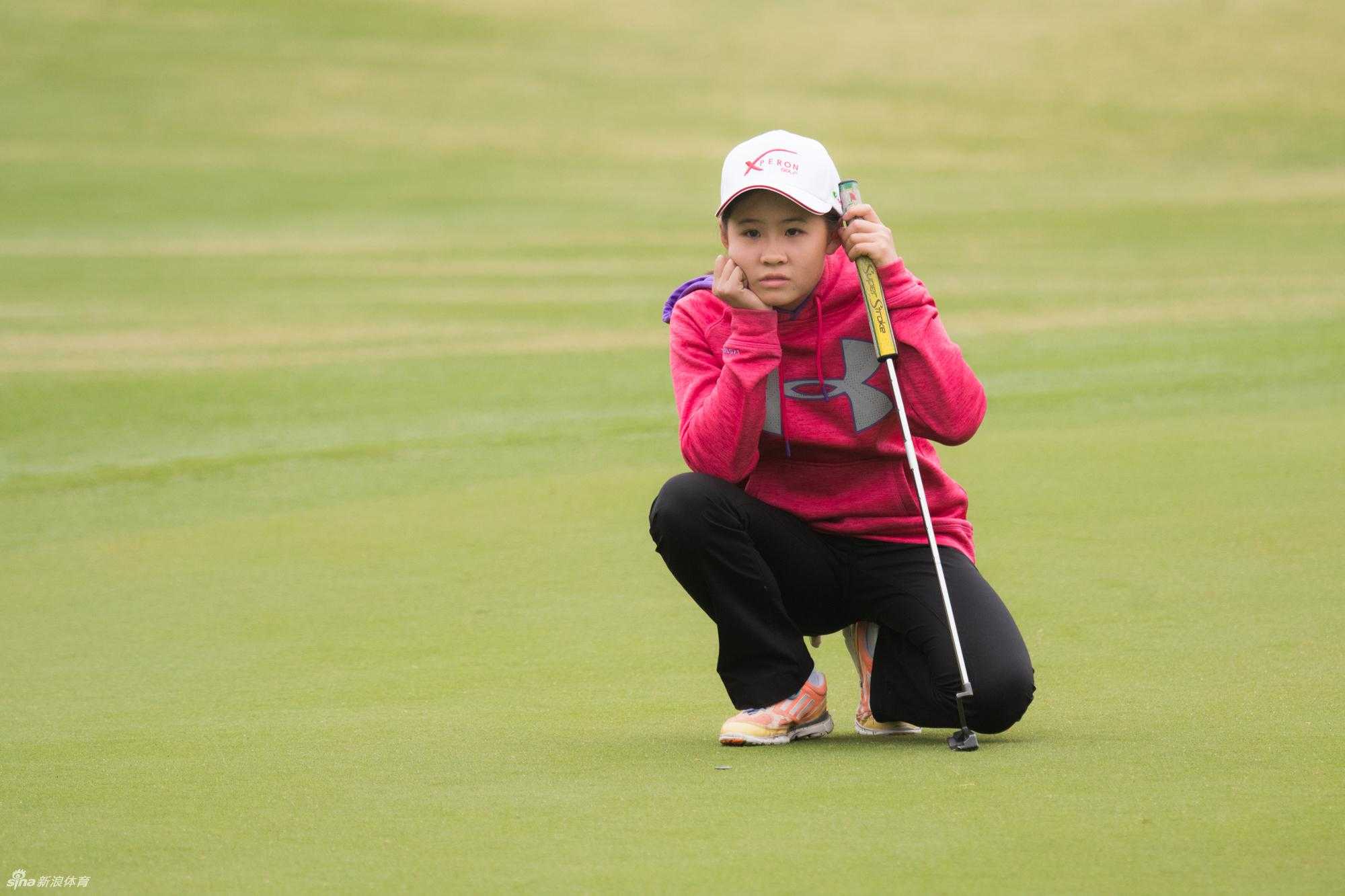 教练正在果岭边对一位小选手进行细致的推杆指导，小选手认真聆听。