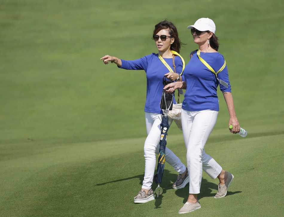 球场边，一位球星女友正专注地用手机记录比赛瞬间，神情认真，体现了现代伴侣的参与方式。