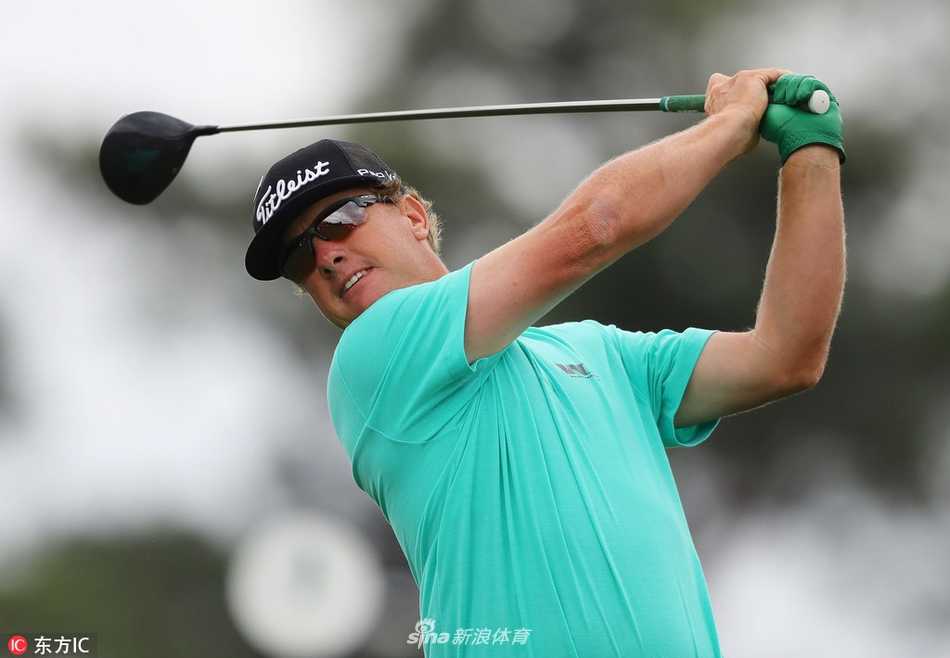 卡梅隆·史密斯微笑着擦拭球杆，身后绿意盎然的球场与他的浅色服装相映成趣