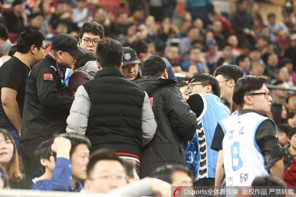 一位身穿深色外套的球迷被身边多人拦住，他仍试图向前冲，脸上的表情写满了愤怒与不甘，周围的观众纷纷侧目，眼神中透露出惊讶与无奈。