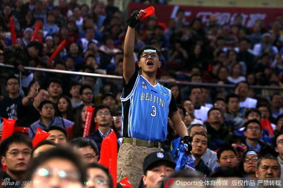 光线昏暗的看台一角，几名球迷越过护栏闯入场地边缘的警戒区，他们背对镜头，目光齐齐投向远处还在理论的人群，现场只剩下混乱的脚步和嘈杂的人声。