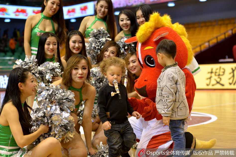 全明星赛场边，小家伙被父亲抱在怀里好奇地张望，身旁的啦啦队姐姐们也被这可爱的‘小明星’吸引，纷纷侧目露出喜爱的笑容。