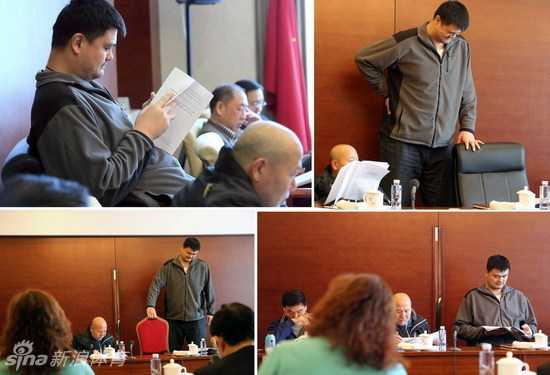 身形高大的姚明蜷缩在为他特制的宽大转椅里，眉头微蹙，似乎正被腰部的不适所困扰，与身旁正常尺寸的桌椅形成鲜明对比。