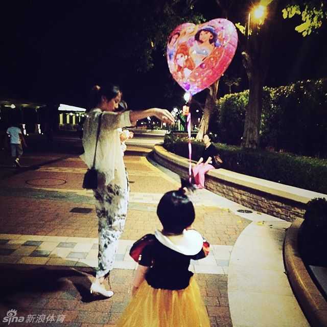 陈露蹲下身子，视线与女儿平齐，耐心地给她讲解着什么。这个小小的动作充满了尊重与平等，母爱的光辉在这一刻比周围的童话布景更加耀眼动人。