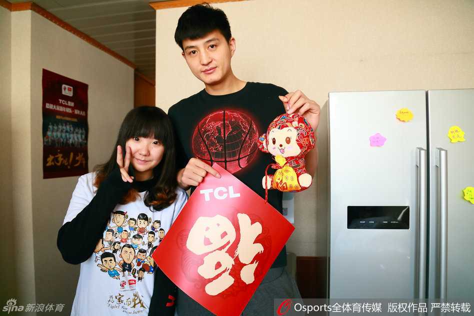 周琦被队友和球迷簇拥在中间，他开怀大笑，笑容极具感染力，整个画面洋溢着喜庆和欢乐的氛围，背景是悬挂着篮球的墙壁。