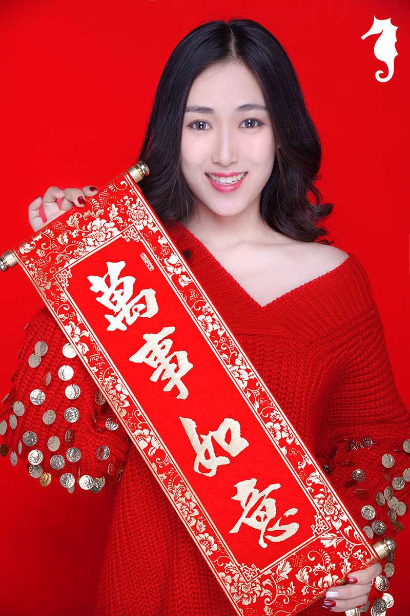 小女孩手捧中国结凑近脸颊嘟嘴卖萌，圆圆的眼睛笑成两道月牙，红扑扑的脸蛋比身上的红装还要娇艳，俏皮又可爱