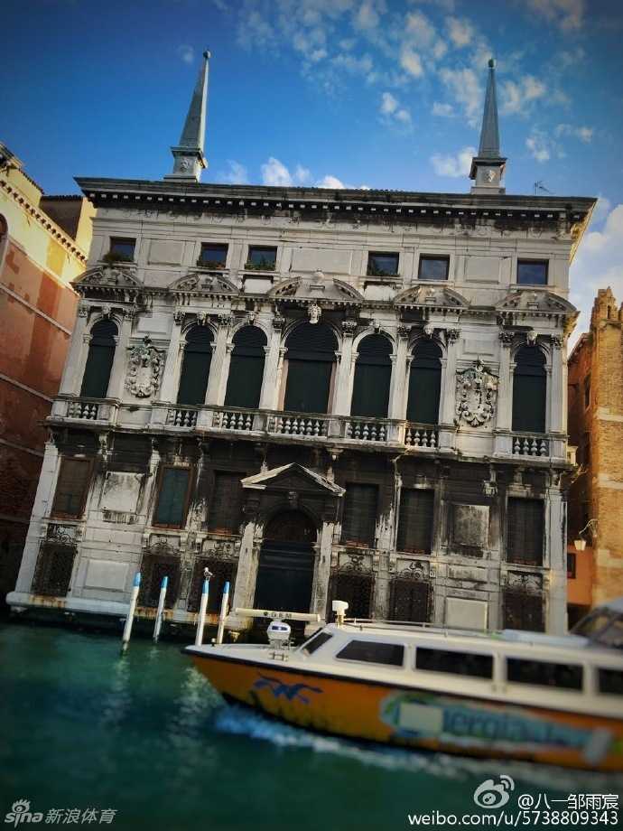 郭艾伦在威尼斯小巷中意外入镜，他手持拍摄设备神情专注，身后是色彩斑斓的威尼斯民居，成为画面中最生动的背景板。