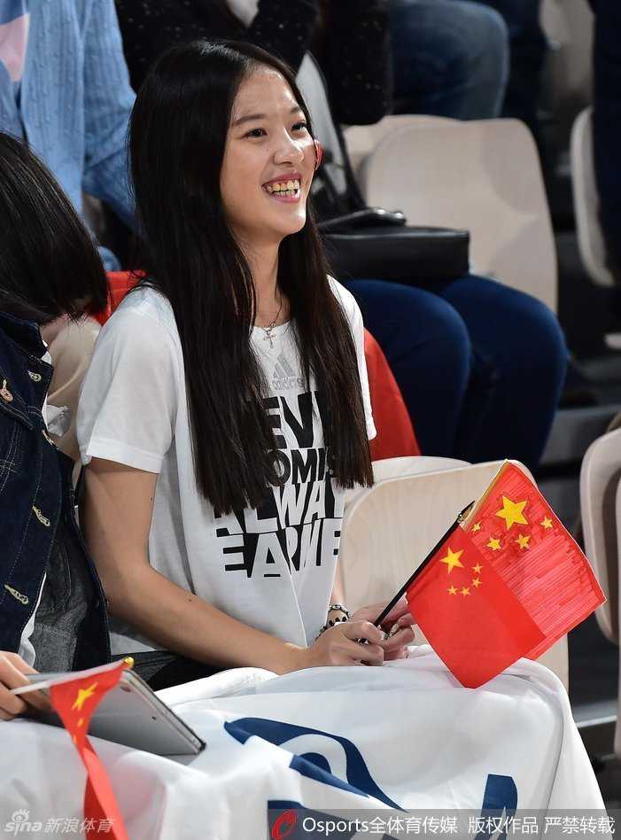 宽阔的体育馆看台上，众多手持五星红旗的球迷已经起身，他们面朝球场，脸上洋溢着紧张而兴奋的神情，仿佛要用自己的呐喊声穿透赛场，为正在进行赛前热身的女篮队员们传递力量。