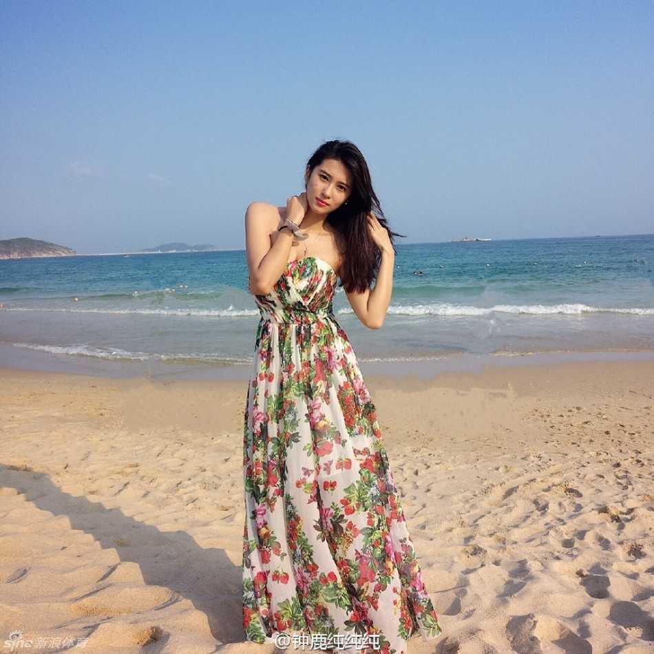 她身穿简约的白色连衣短裙，漫步在沙滩上，修长的双腿在蓝天碧海的映衬下显得格外耀眼，恰似一道流动的风景线。