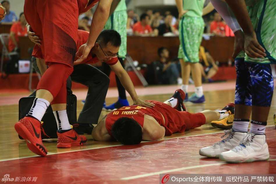 男篮热身赛惊魂一刻:周琦意外受伤痛苦倒地,队友揪心队医紧急治疗 回到场边的周琦坐在板凳席上,队医仍在为他进行细致的检查和处理。周琦低头看着自己的伤处,神情落寞,身旁的队友们也神色凝重,默默关注着他的情况。