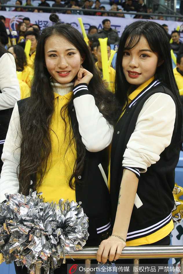 背对镜头的篮球宝贝，单手高举过头顶比出数字一的手势，紧身短裙勾勒出优美的身体线条，舞台灯光在她的肌肤上洒下柔和的光晕，动感中透着性感。