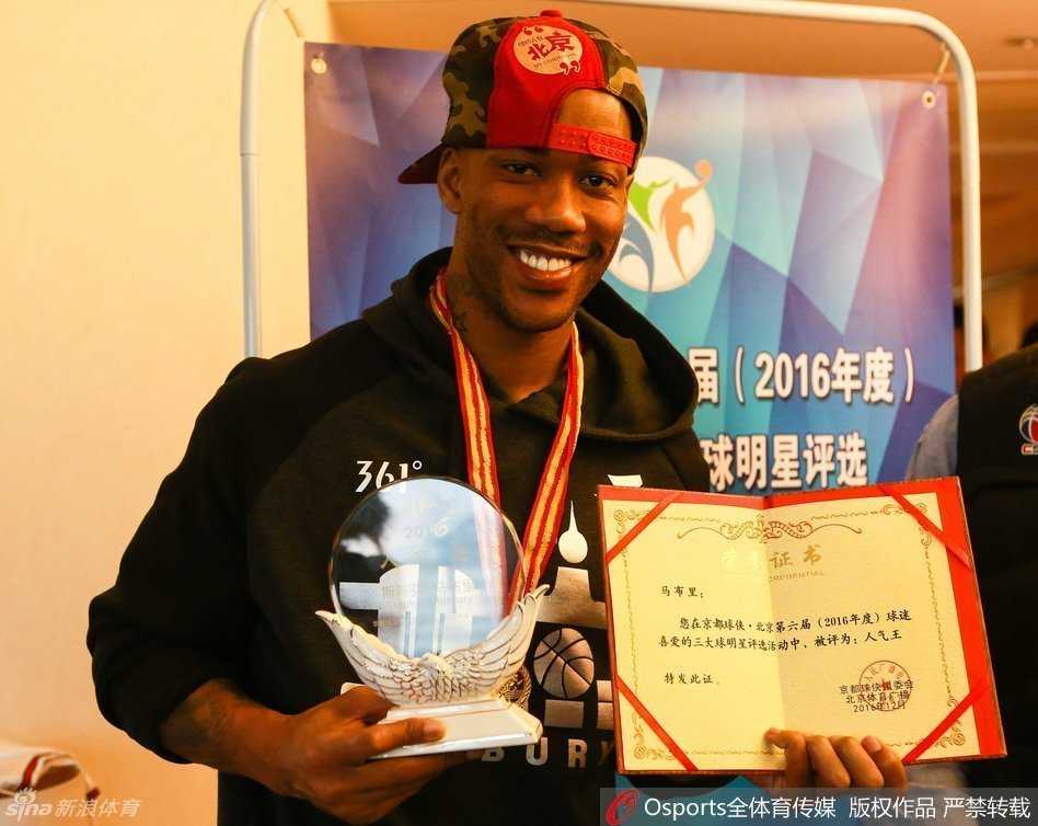 在北京的家中，马布里与徐济成并肩而坐，两人微笑着翻阅一本记录着老马北京生涯的相册，墙上挂着的书法作品更添几分家的温馨。