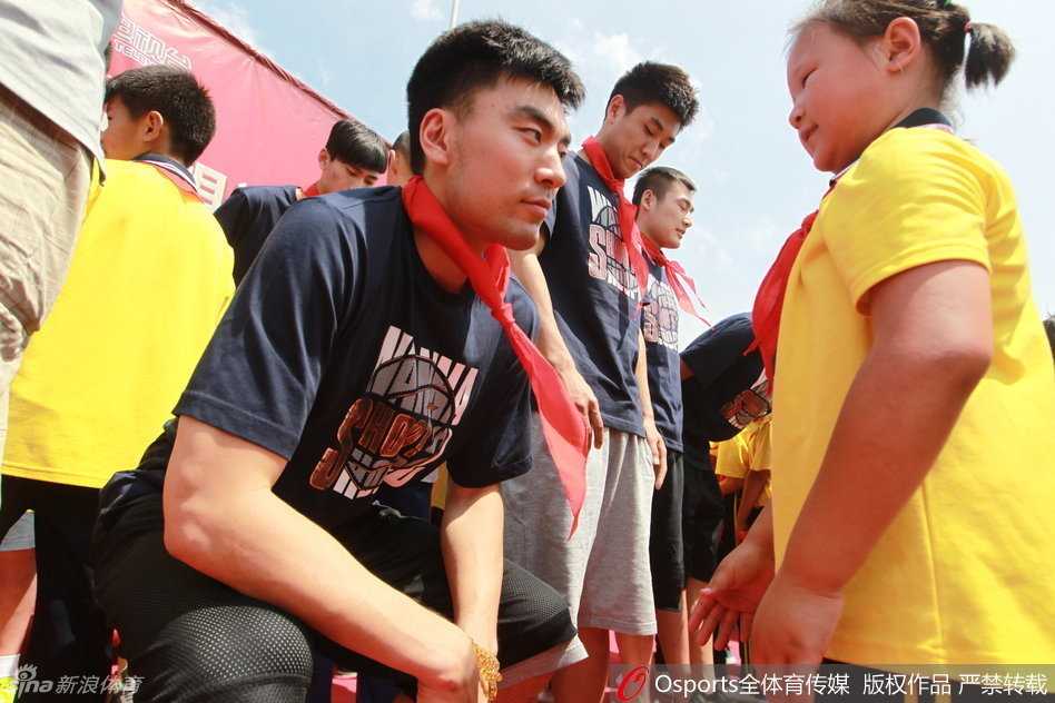 在简陋的篮球架下，李晓旭俯身与一名小朋友亲切击掌，鼓励他在球场上要勇敢和自信，身后是围观同学们开心的笑容。