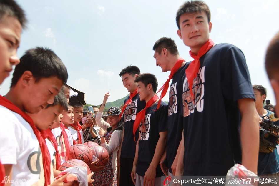 一名小学生踮起脚尖，认真地为李晓旭系上鲜艳的红领巾，李晓旭则像大哥哥一样配合地弯下腰，画面温馨有爱。