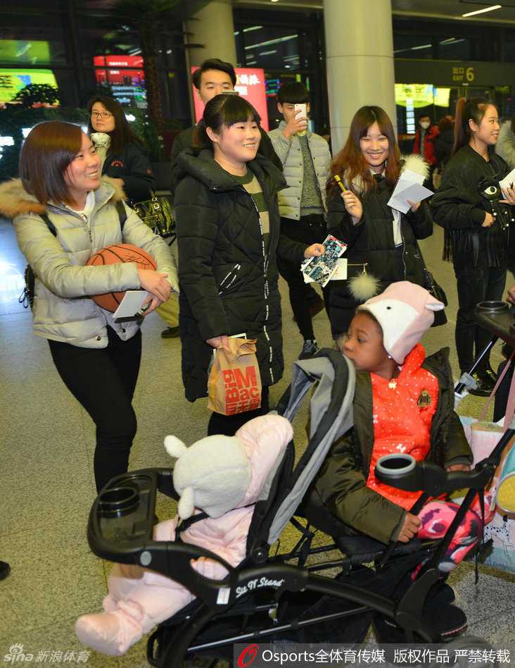 辽篮将士载誉返沈 哈德森小公主萌翻接机现场 哈德森的女儿坐在婴儿车里,身穿粉色棉衣,头戴毛线帽,圆嘟嘟的脸蛋上挂着好奇的笑容,小手伸出车外,萌态可掬。