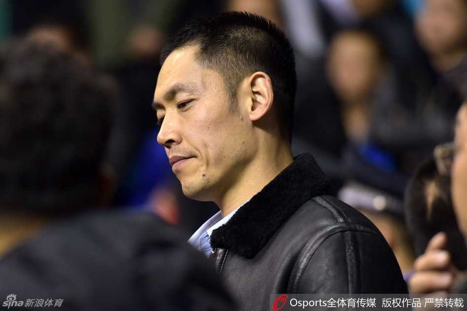 张庆鹏坐在场边观众席上，面带微笑，眼神专注地看着场内，他身穿便装却难掩运动员的挺拔气质，身边的朋友正与他交流着场上的局势。