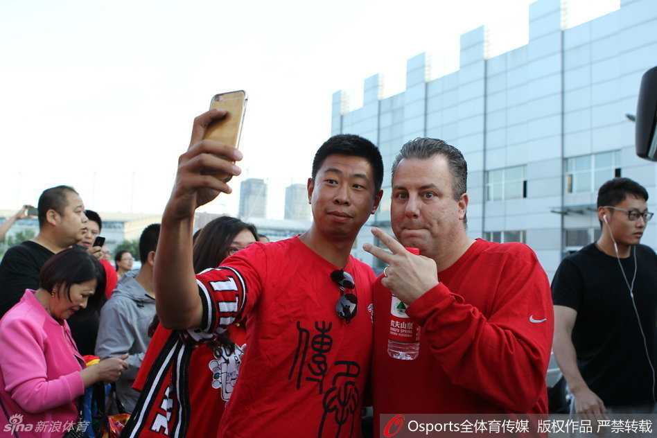 邓华德在看台上做出标志性的胜利手势，眼神中透露出对胜利的渴望，嘴角挂着标志性的邓式微笑。
