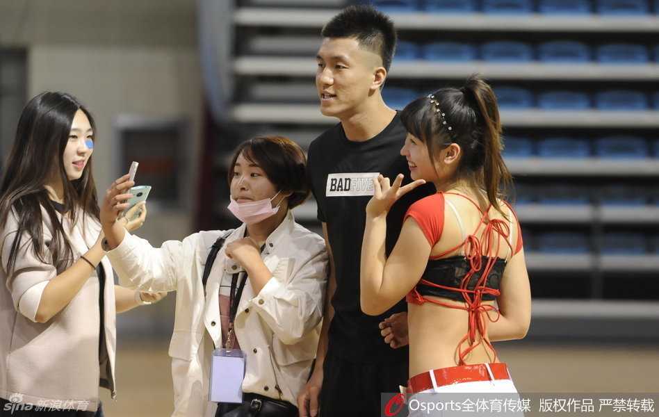 郭艾伦面带微笑地站在展厅中央，身旁围绕着几位兴奋的女球迷，他微微侧身配合她们拍照，眼神中满是宠溺与温柔。