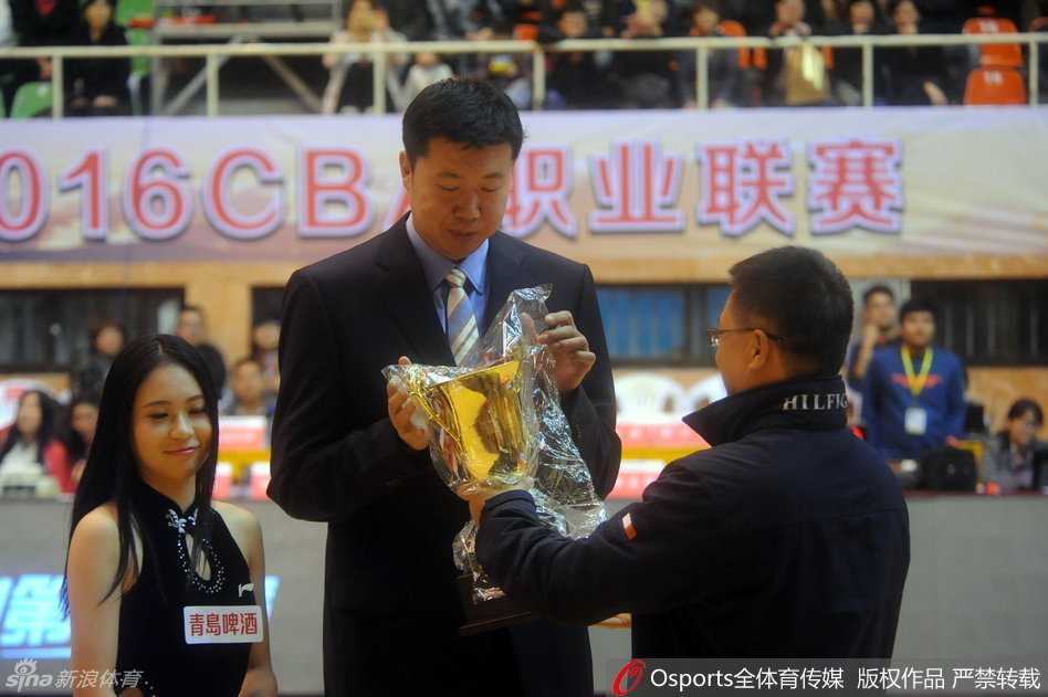 在比赛现场的背景板前，王治郅与一位优雅的女嘉宾共同捧着奖杯合影，记录下这历史性的瞬间，标志着一位传奇球员职业生涯的圆满落幕。