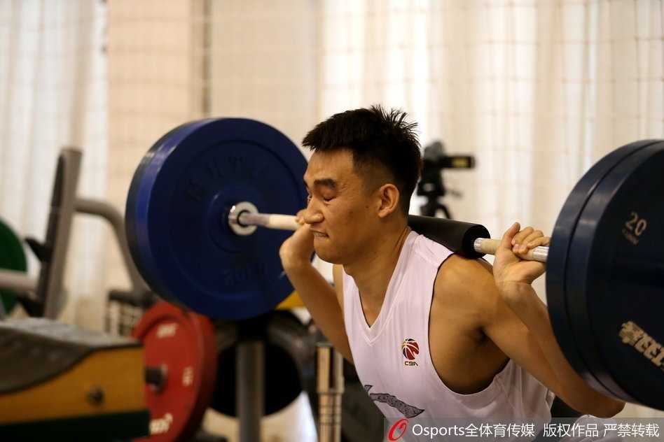 测试现场，一名球员正在保护人员的协助下完成深蹲的最后锁定阶段，汗水已经浸湿了他的球衣，展现出极高的专注度。