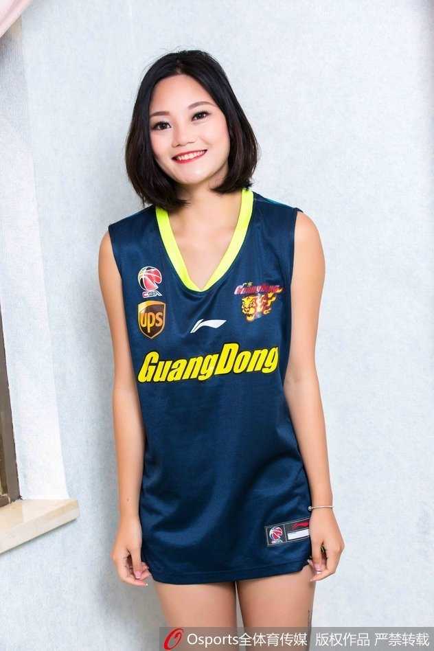 女孩蹲坐在场边的广告牌旁，单手托腮，宽松的球衣下露出灿烂的笑容，甜美可爱的气质成为赛场边的一抹亮色。