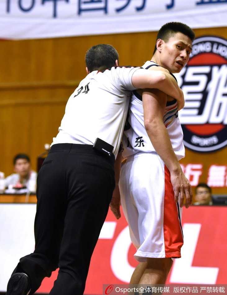 裁判员奋力挤进人群中央，双臂张开用身体隔开冲突的球员，他眉头紧锁神情严肃，身后是情绪失控的球员被队友死死抱住，现场一片混乱。