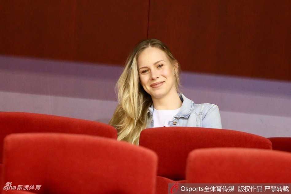 莫泰妻子在场边神情微动，似乎正为场上一次激烈的身体对抗而揪心，金色的发丝在顶灯的照耀下泛着微光。