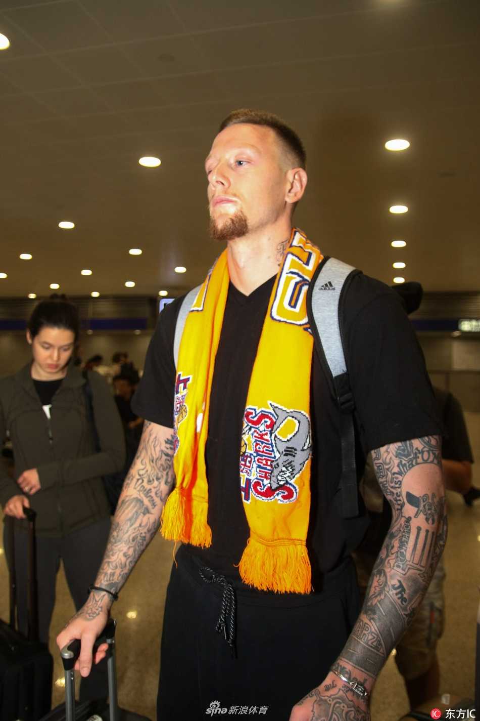 明纳拉斯在机场接受采访，他手持话筒神情专注而放松，身边的新婚妻子则以温柔的目光注视着他，画面充满了温馨与信任感