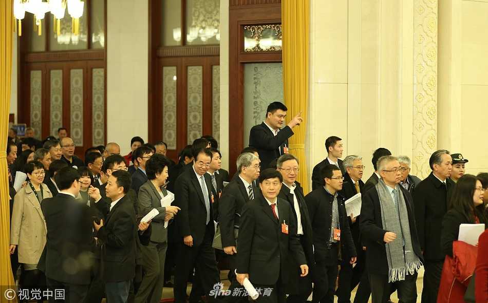 站在人民大会堂宽阔的楼梯间，姚明与王励勤被几位同行的代表委员围住，大家利用休会间隙热络地交谈，姚明微微低头倾听，展现出谦逊而专注的履职姿态。