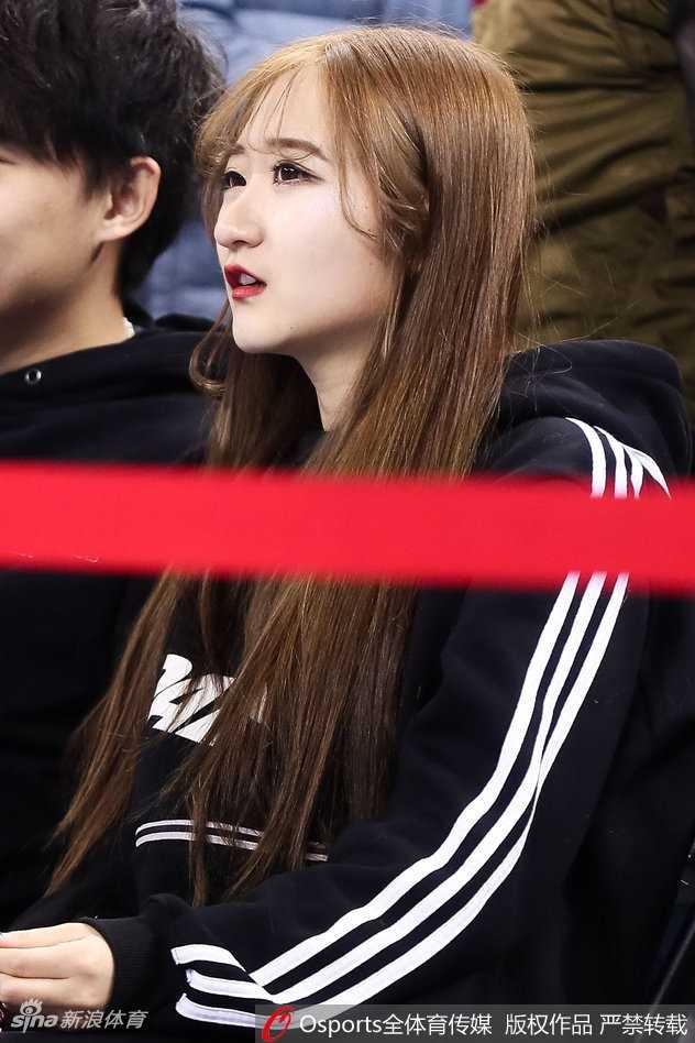 长发披肩的女生轻倚在栏杆旁，唇红齿白，眉眼间带着浅浅的笑意，她像是从画中走出的校园学姐，恰好路过这片热血沸腾的战场。