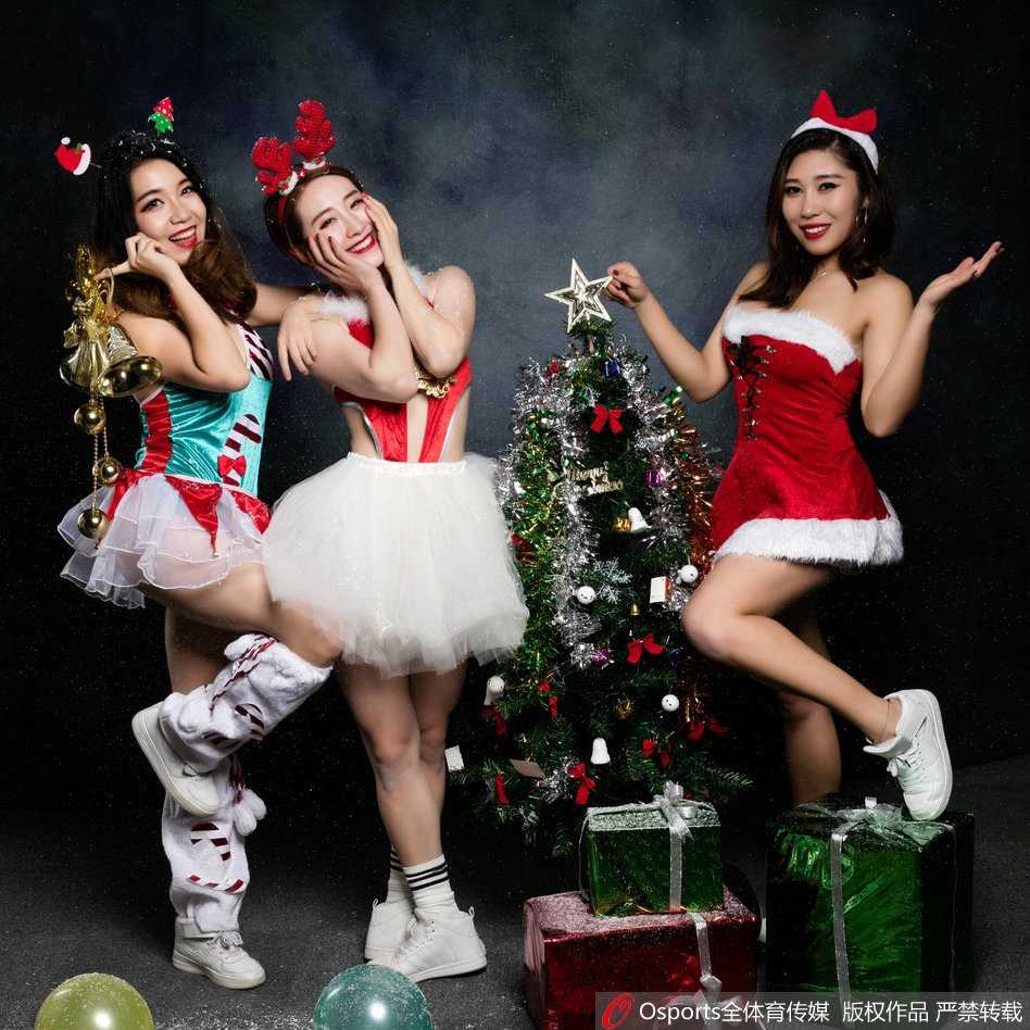 一位篮球宝贝安静地站在巨大的金色圣诞树前，双手交叠，笑容温婉，背景的灯光映衬出她柔美的轮廓，画面静谧而温馨。