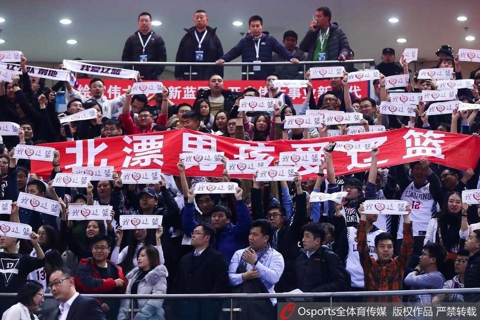 一位辽宁女球迷在人群中格外显眼，她脸上画着辽宁队的队徽，双手攥成拳头放在胸前，眉头紧锁，目光焦虑却又无比坚定地盯着赛场