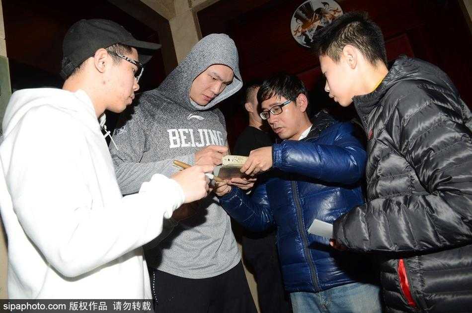 京旅抵沪人气旺,翟晓川携“双星”为球迷签名合影 翟晓川身穿蓝色休闲装,面带阳光微笑低头为小球迷签名,周围人群举起手机记录这追星时刻