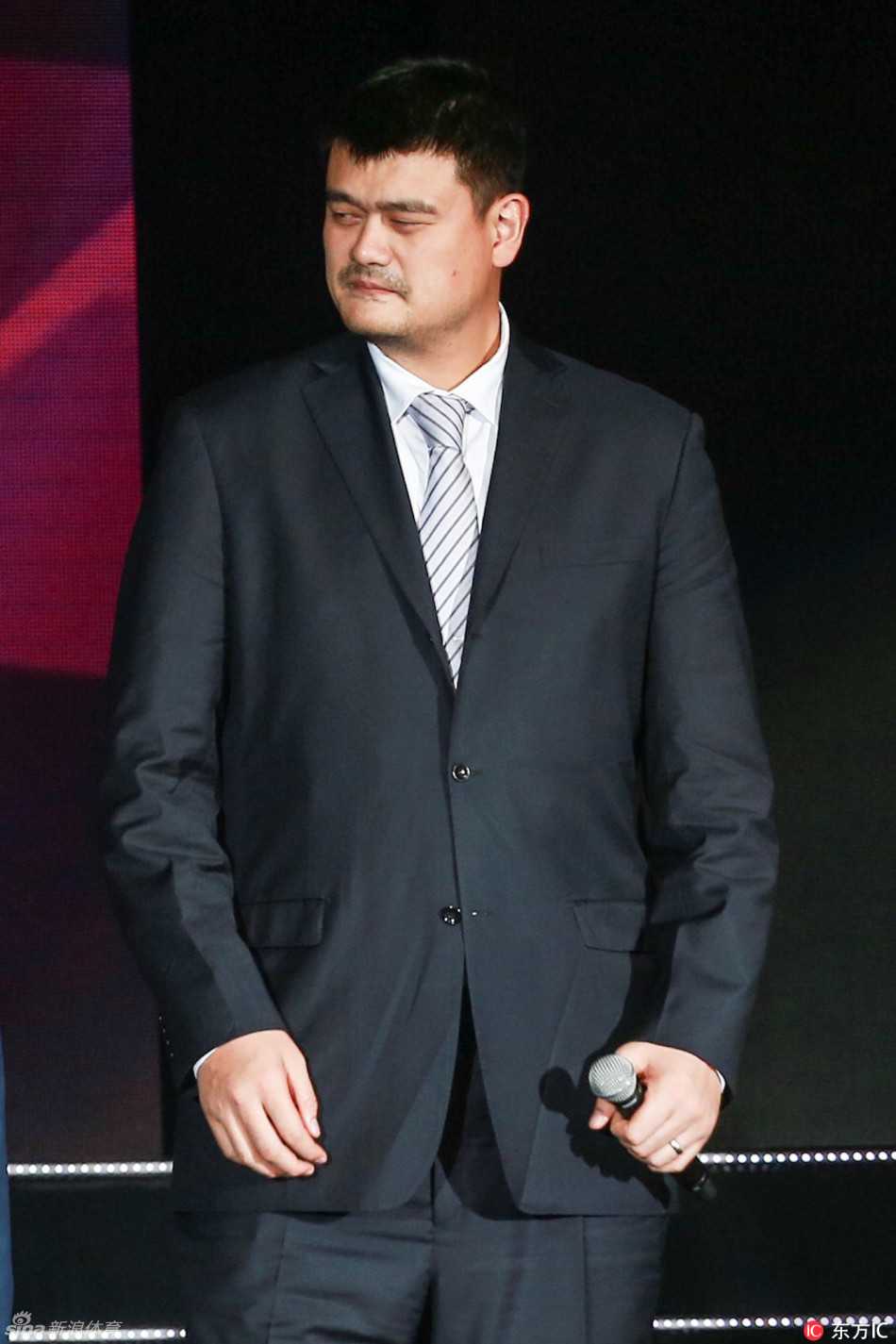 篮球场边，姚明身着笔挺西装认真观战，眼神锐利仿佛仍在思考战术，即使坐在场下也带着曾经赛场上的威严。