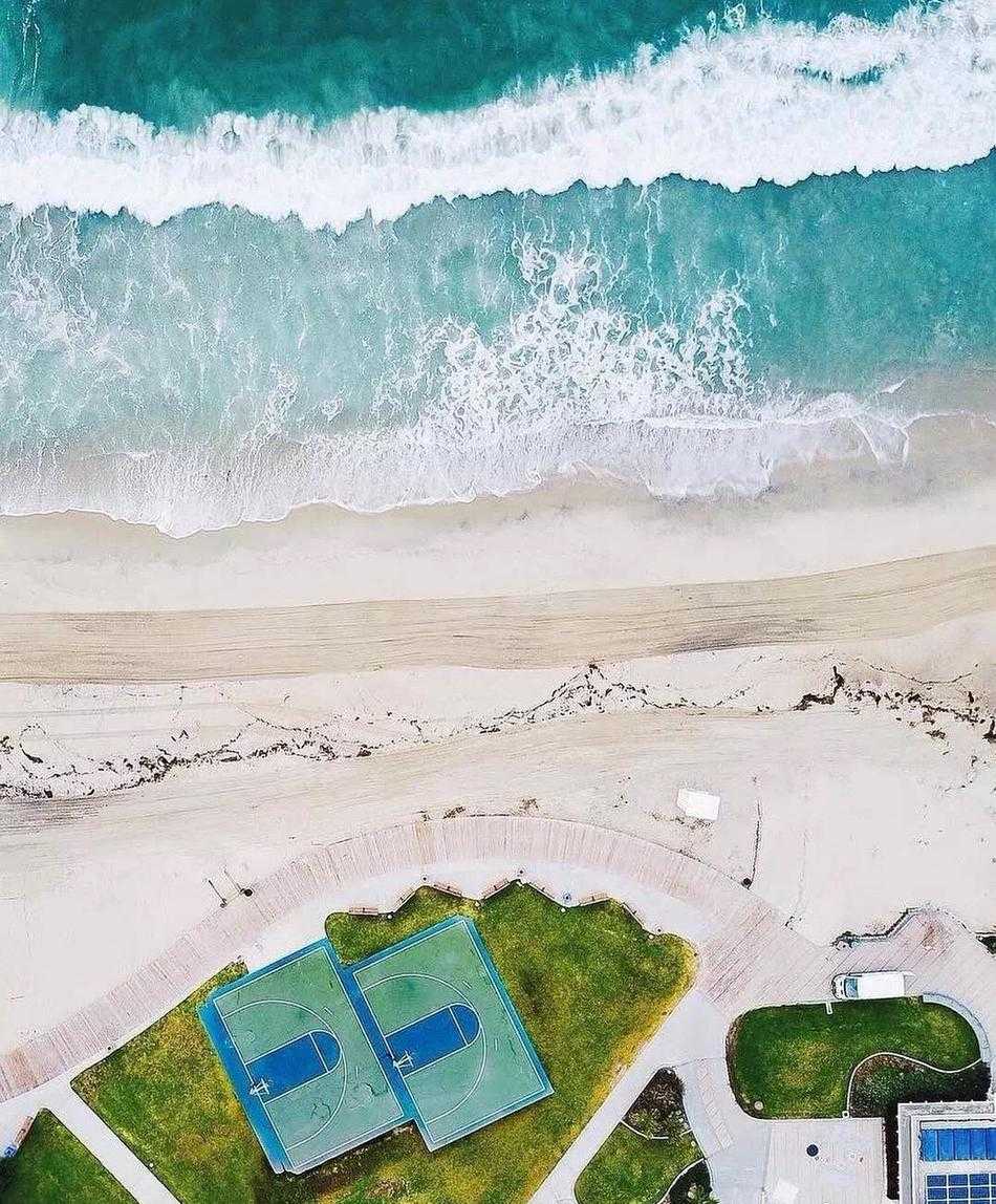 俯瞰光影交错,探寻篮球场的几何诗意 夕阳西下,阳光斜射进室内篮球馆,高大的落地窗、光洁的木地板和远处的篮筐构成一幅宁静深邃的纵深感画面。