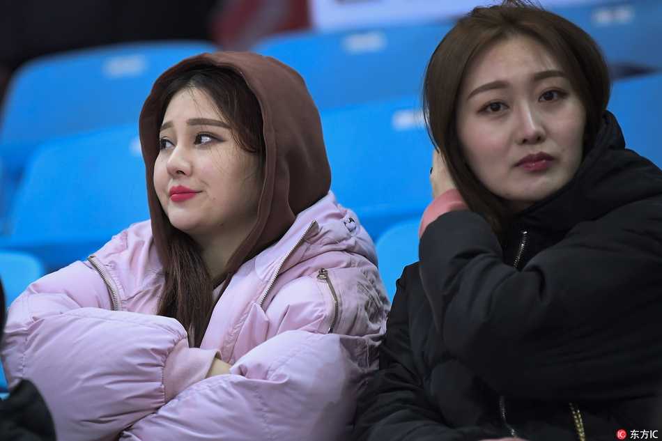 身穿白色短款羽绒服的清纯女生，手拿吉林东北虎的加油棒，眼神清澈地望向赛场方向，嘴角带着浅浅的笑意，仿佛对主队充满信心