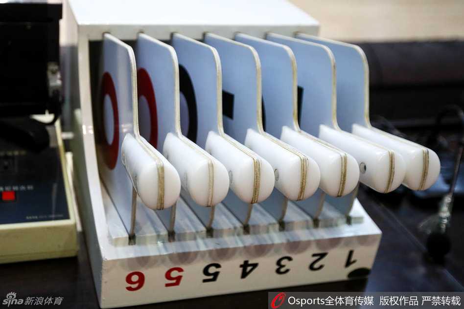 红色的犯规牌被一只手持握着，准备插入全队犯规显示器的卡槽中，背景是模糊的技术台仪表盘，这抹鲜艳的红色如同警戒线，提醒着即将上场的球员们注意防守动作的尺度。