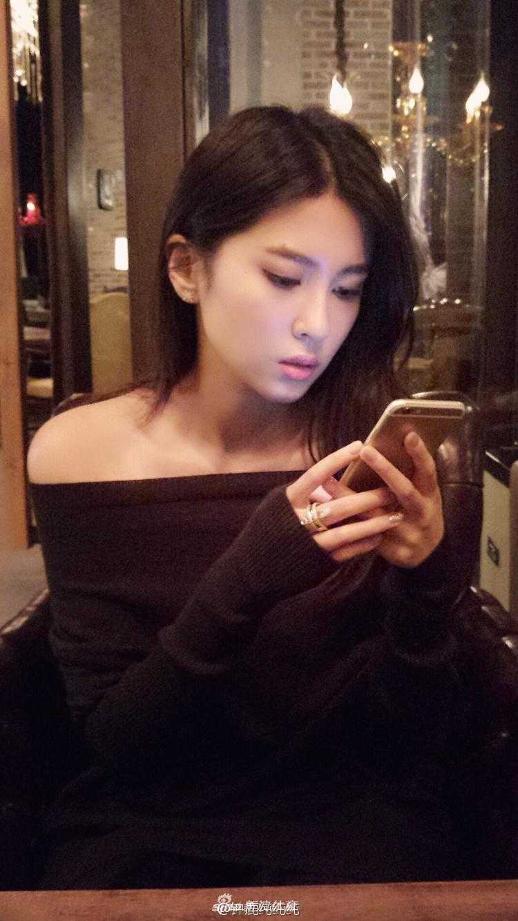 钟鹿纯身穿黑色露肩连衣裙，展现出迷人的锁骨和香肩，面对镜头露出甜美自信的微笑，气质高贵而迷人。