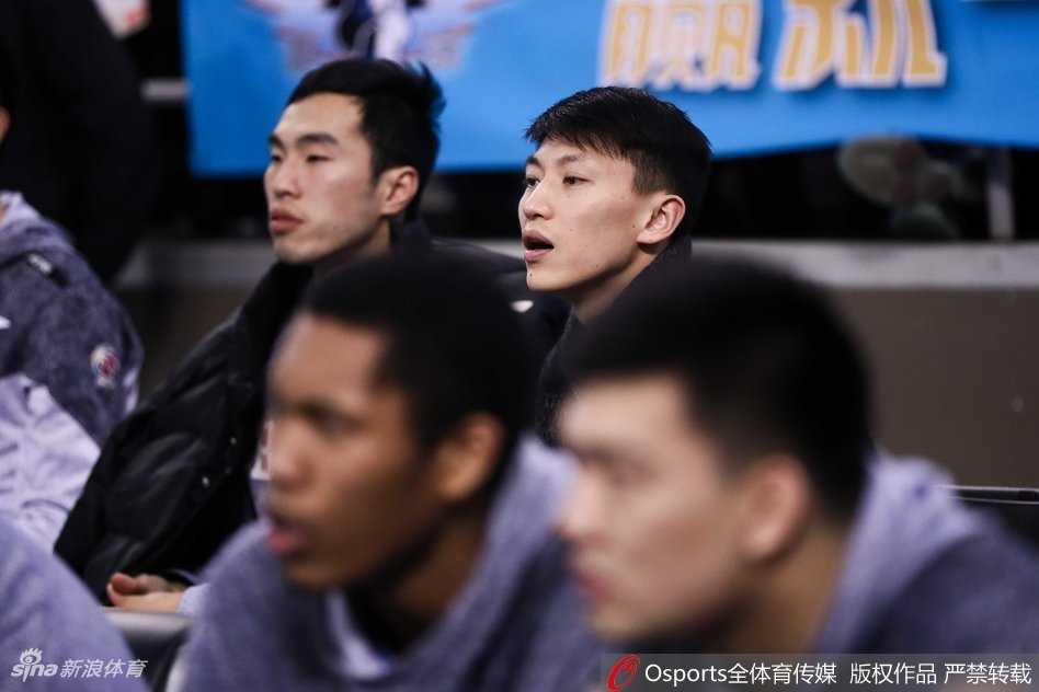 刘晓宇仰头看着球场上方的大屏幕，屏幕上闪烁着比分和时间，他的眼神中带着思考，仿佛在模拟如果自己在场上会如何处理球。